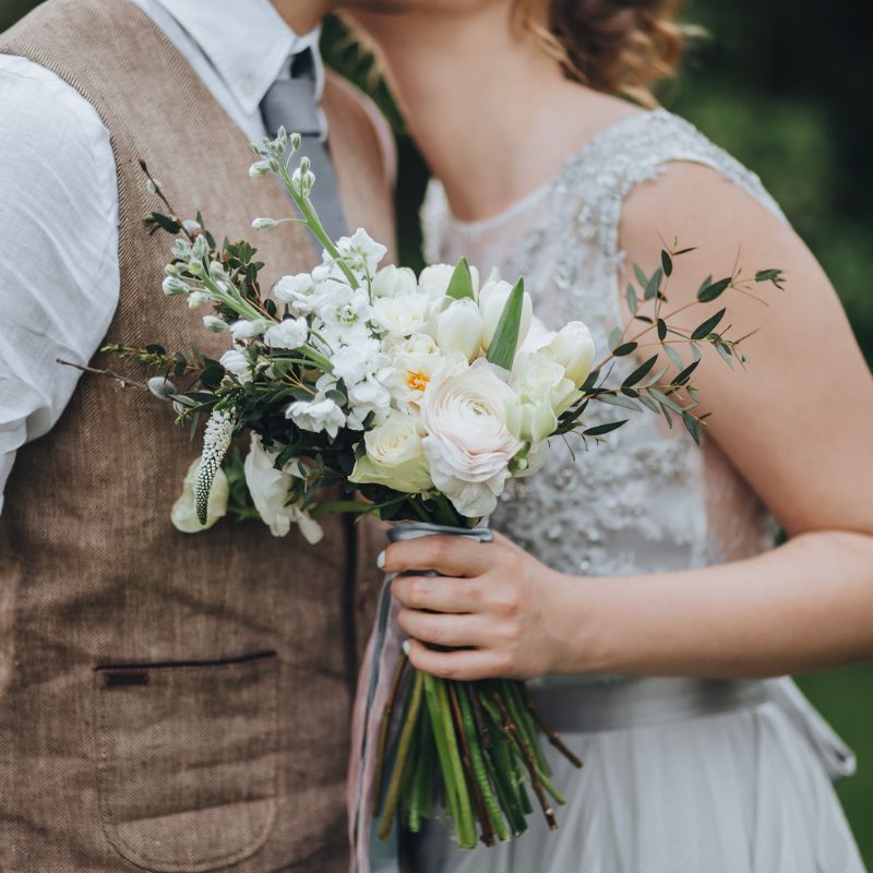 Wedding photo with groom in tan vest and bride holding small bouquet outside.